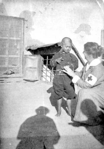A nurse in a cross armband examines a child. Harpoot, c. 1919-1922.