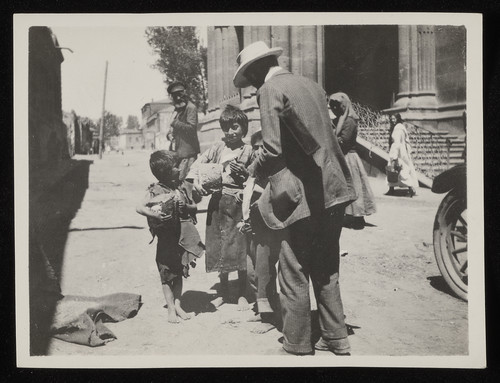 Man in white hat, possibly Jaquith, handing bread to boys, Caucasus, 1920s