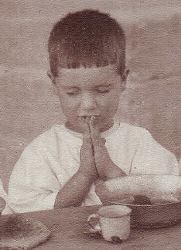 Antranig Karjian says grace over a bowl and tin cup at the Birds' Nest Orphanage, Sidon, c. 1921–1923.