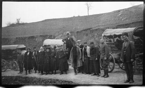 A travel party of relief workers in ACRNE uniforms and service stars halts with covered carts on a road below a bare hill, near Karakilisse (Vanadzor), Armenia.